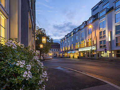 Vista exterior nocturna del Maritim Hotel Würzburg con fachada iluminada y un antiguo portal al fondo