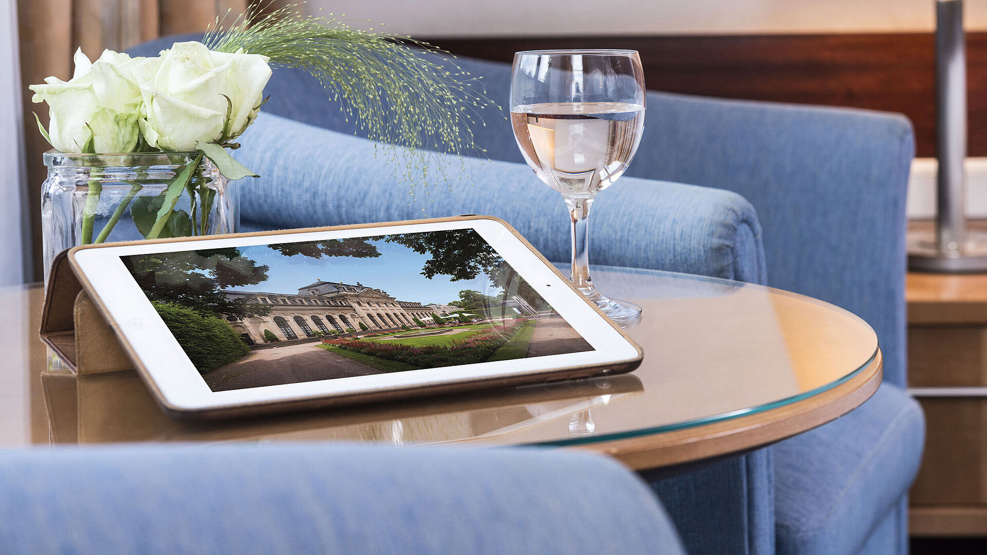 Accogliente area relax al Maritim Hotel Fulda con tablet, bicchiere d’acqua e rose bianche su tavolo in vetro.
