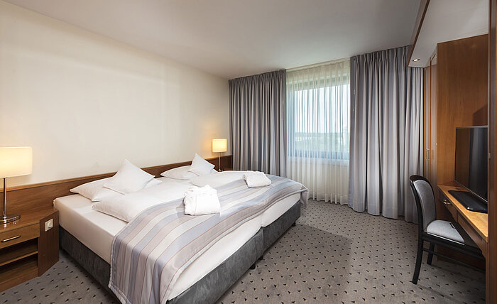 Junior Suite con cama doble cómoda, TV, escritorio y grandes ventanas en Maritim Hotel Hannover.