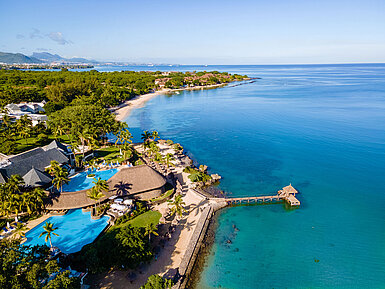 Aerial view of a beach resort with pool, palm trees and direct access to turquoise sea