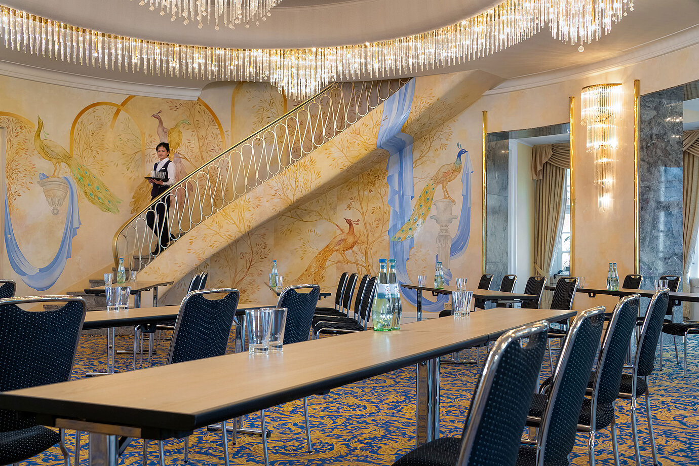 Fürst-von-Pückler Hall with row seating, artistic wall design, large staircase and staff member on the stairs.