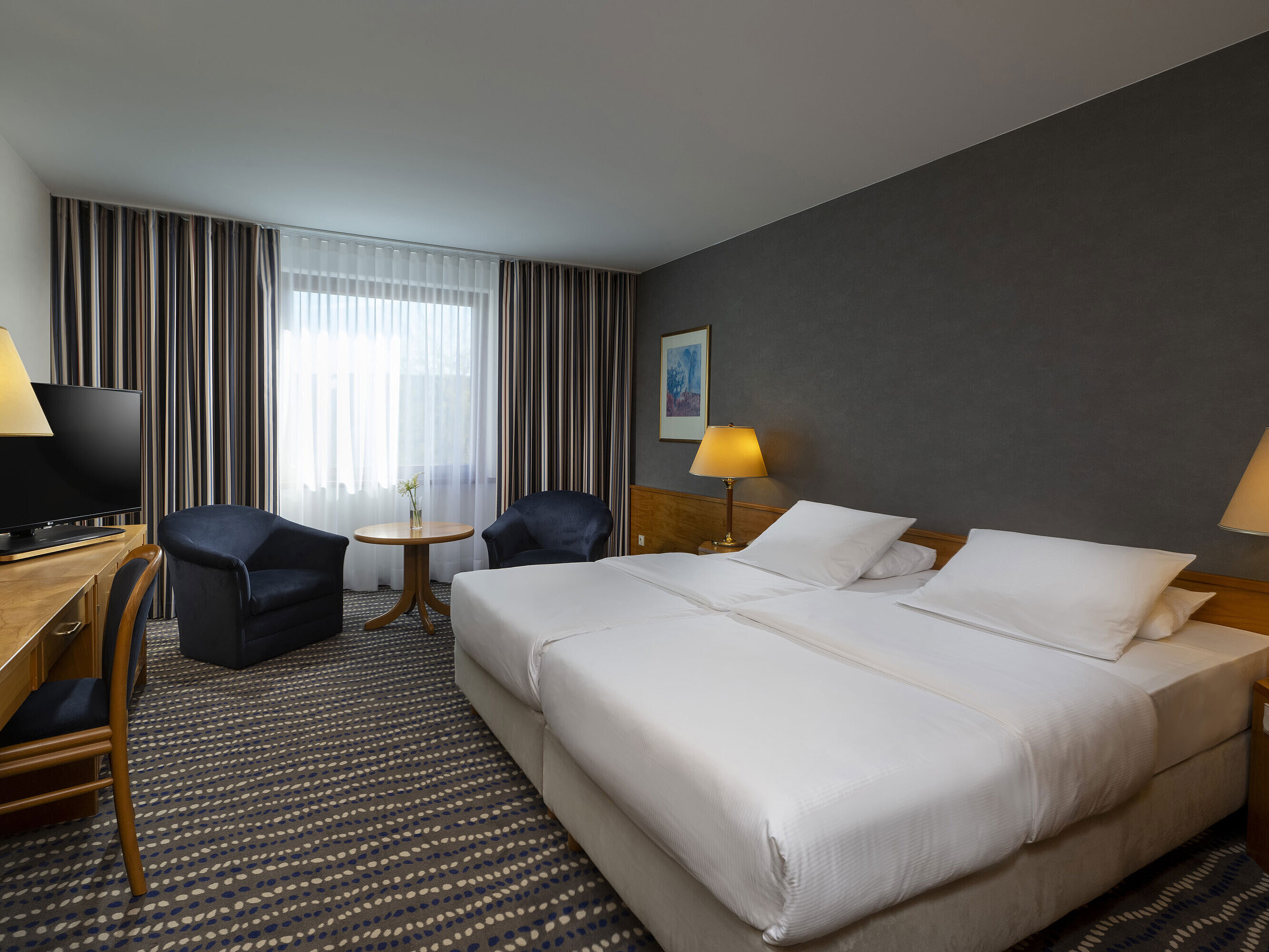 Camera d'hotel con letto matrimoniale, TV, scrivania e angolo salotto accogliente, ideale per relax e comfort