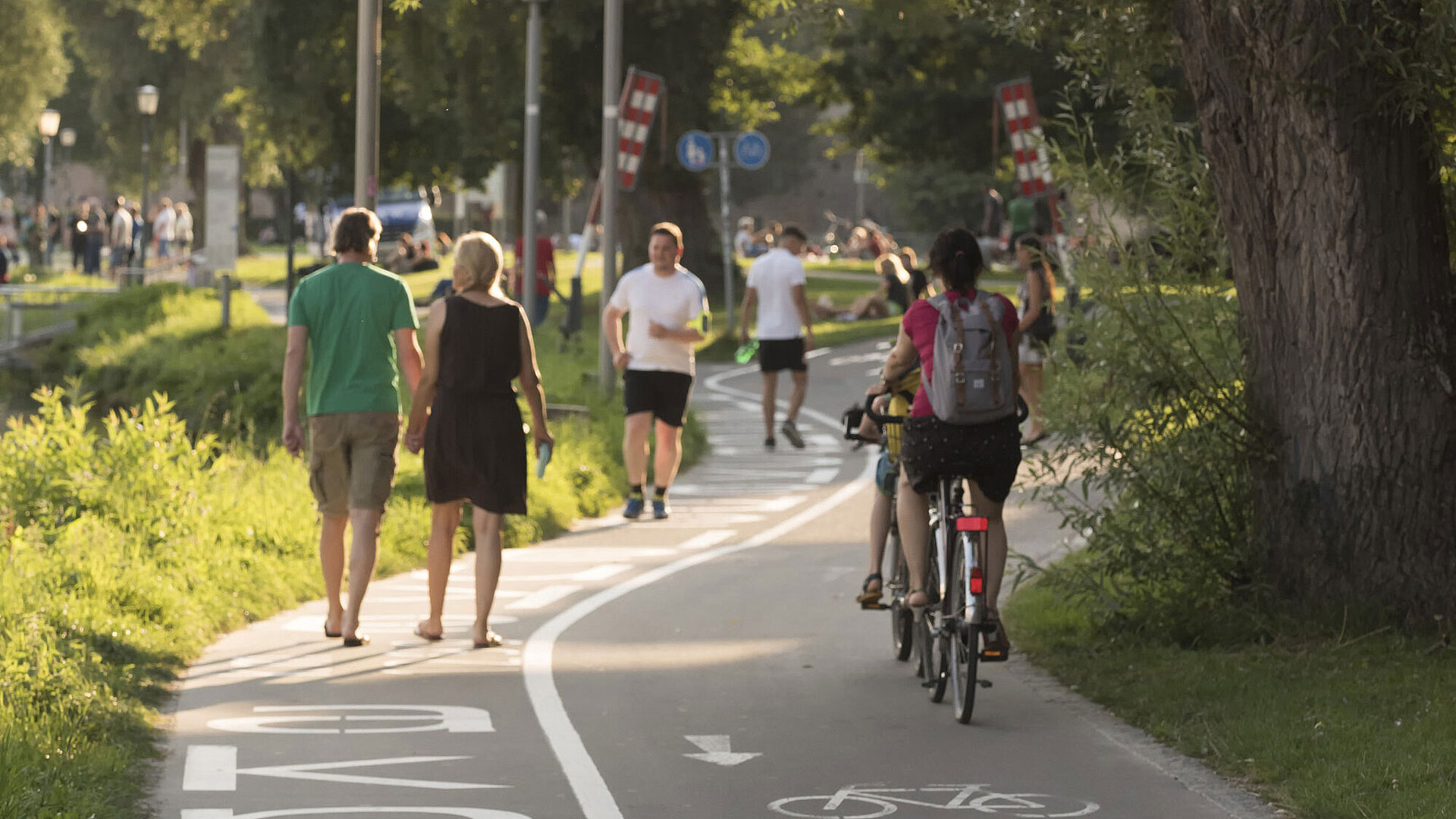 Pedestrians and cyclists on the Danube promenade in Ulm under the summer sun.