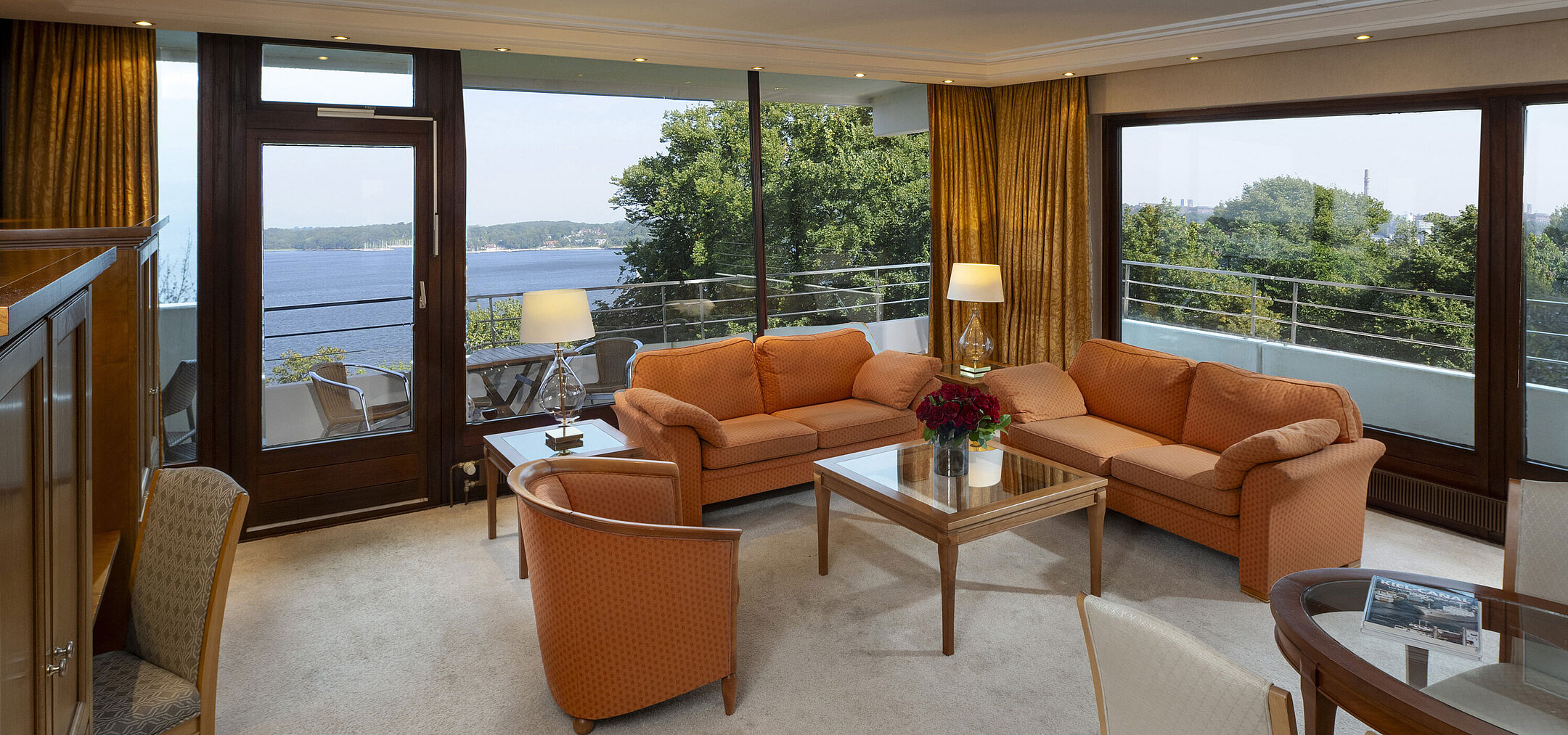 Sala de estar luminosa de la suite presidencial en el Maritim Kiel con vista panorámica al mar Báltico y muebles elegantes.