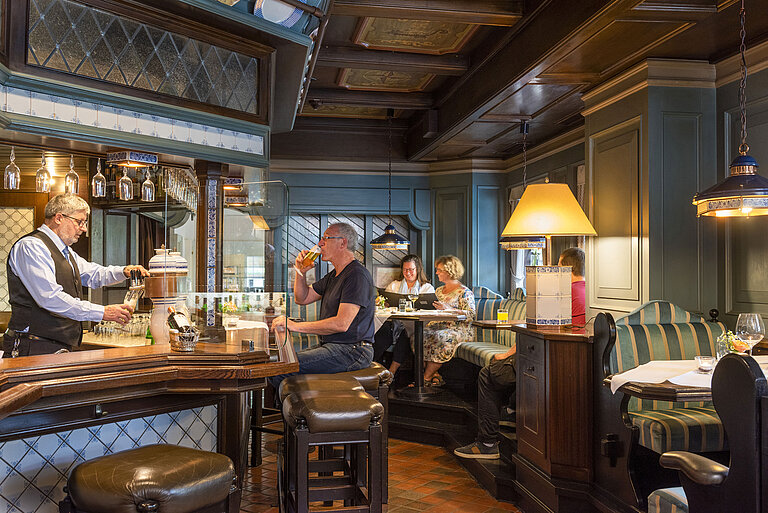 Bar d'hôtel confortable de style traditionnel avec des clients profitant de boissons et un barman servant de la bière.