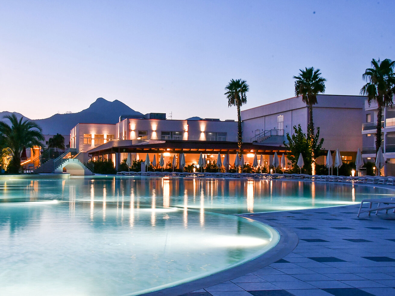Luci serali alla piscina del Maritim Resort Calabria con palme e montagna