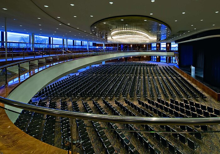Amplio salón de eventos en el Maritim Hotel Düsseldorf con asientos en fila y una elegante galería para conferencias y eventos.