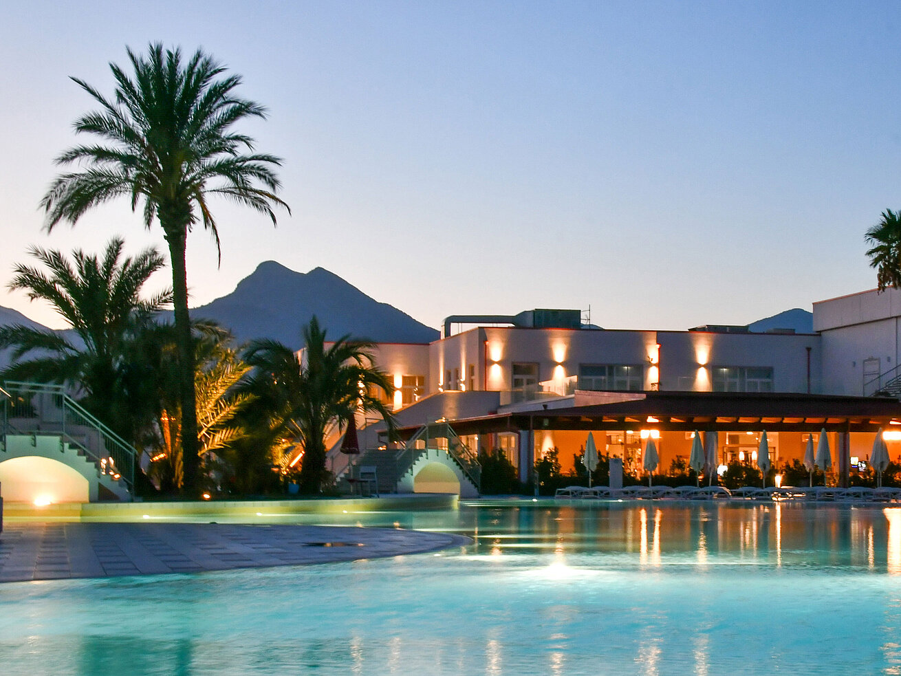 Evening lights at the pool of Maritim Resort Calabria with palm trees and mountain backdrop