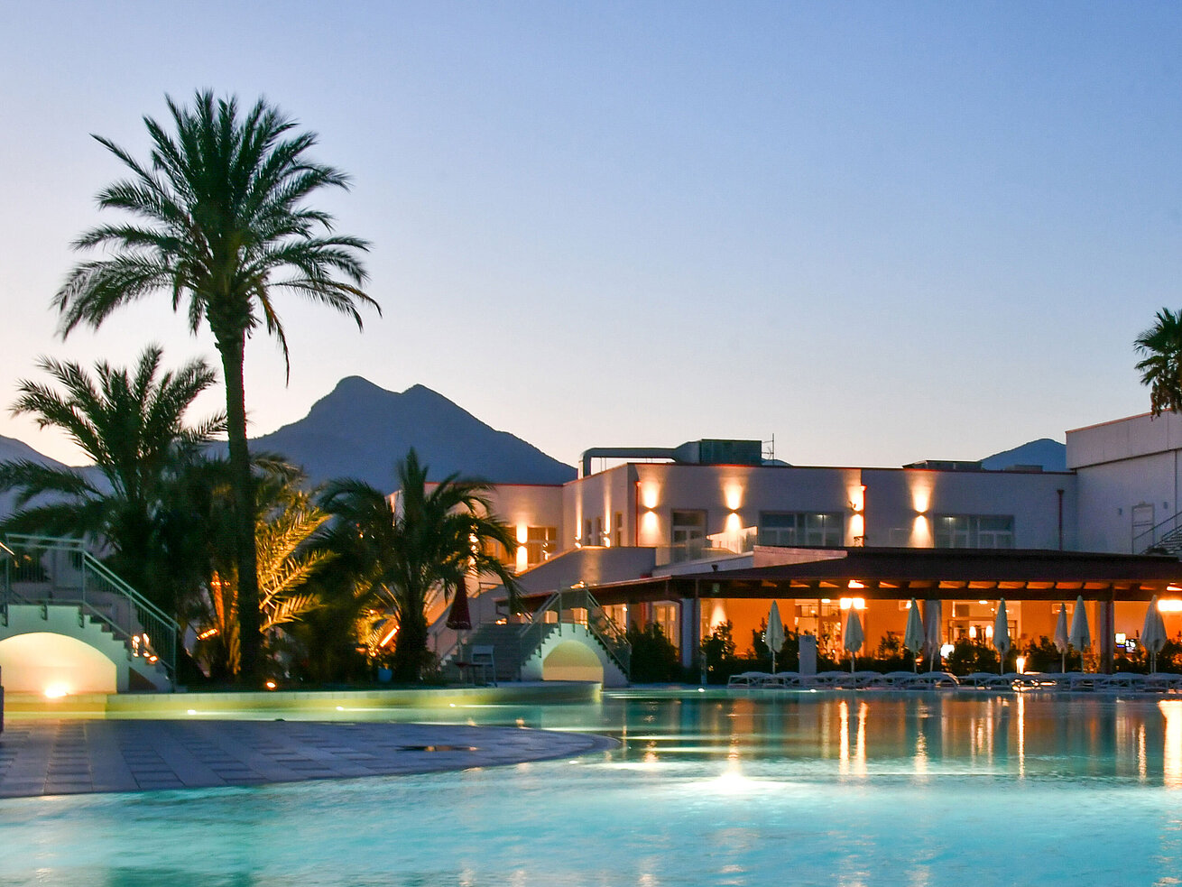 Pool Evening lights at the pool of Maritim Resort Calabria with palm trees and mountain backdrop