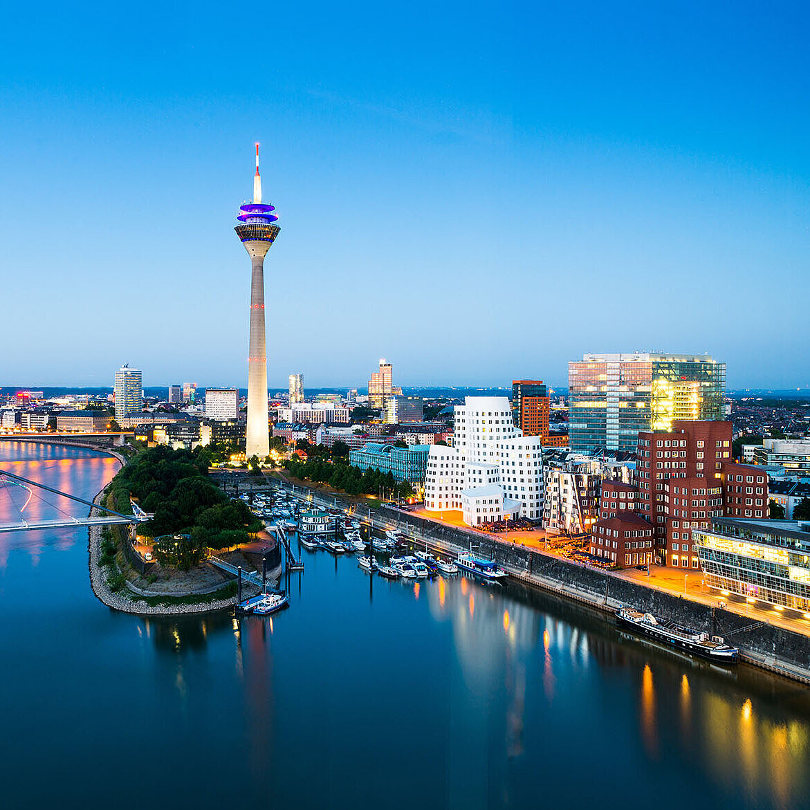 © conorcrowe - AdobeStock.com Dusseldorf skyline with the Rhine Tower, riverside promenade and modern architecture at dusk.