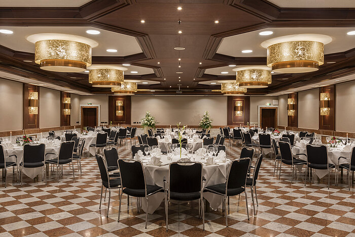 Élégante salle de banquet au Maritim Hotel Königswinter avec tables rondes, décor raffiné et lustres.