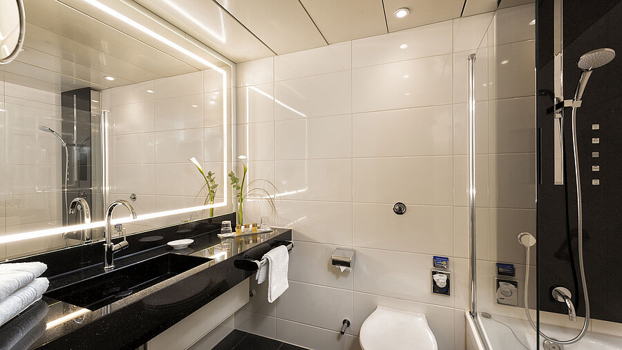 Baño moderno con ducha y bañera en el Hotel Maritim Bonn, con elegantes accesorios y espejo iluminado.