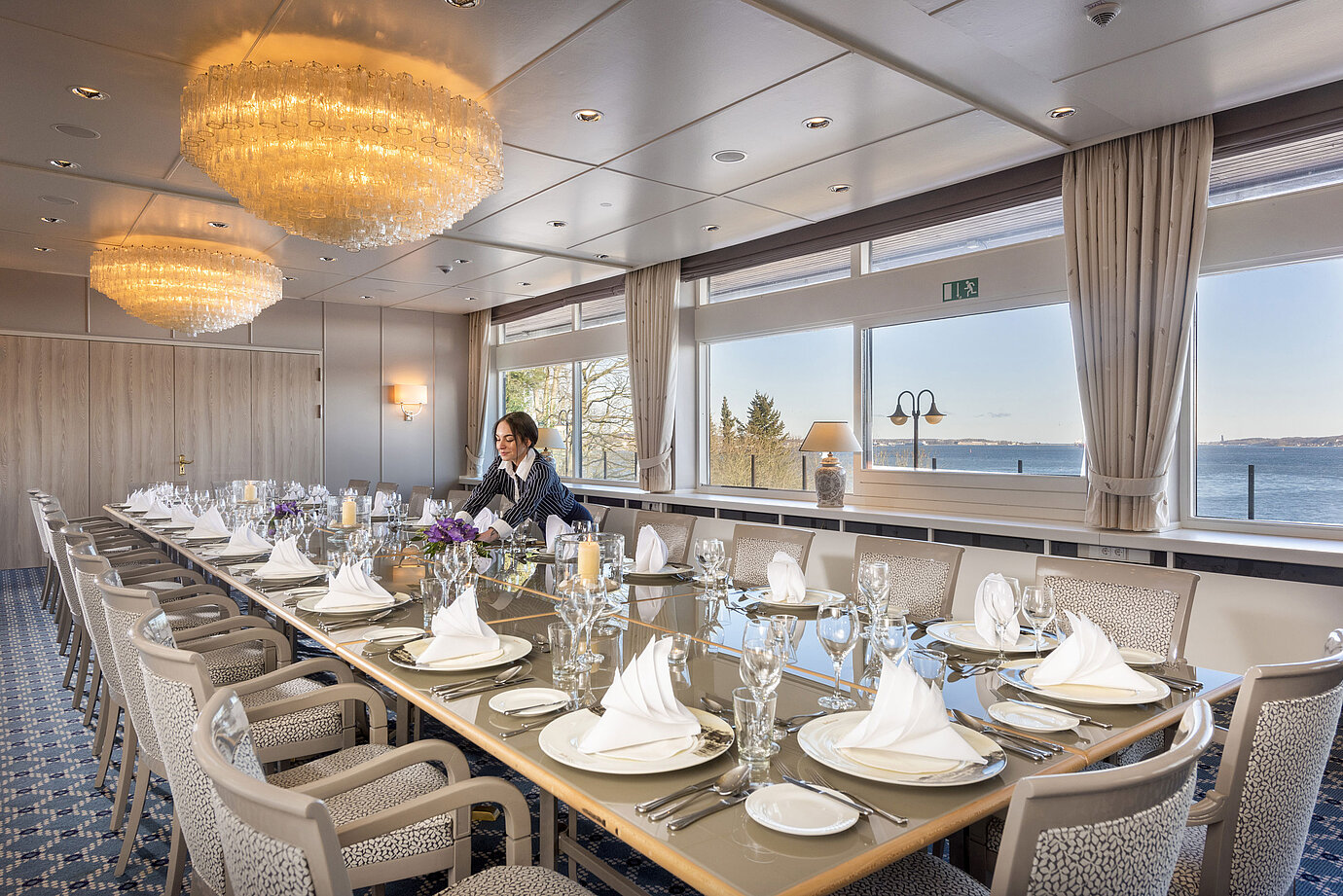 Salone Oslo nel Maritim Hotel Kiel, lunga tavola imbandita a festa con vista sul mare, lampadario, personale che sistema la sala.