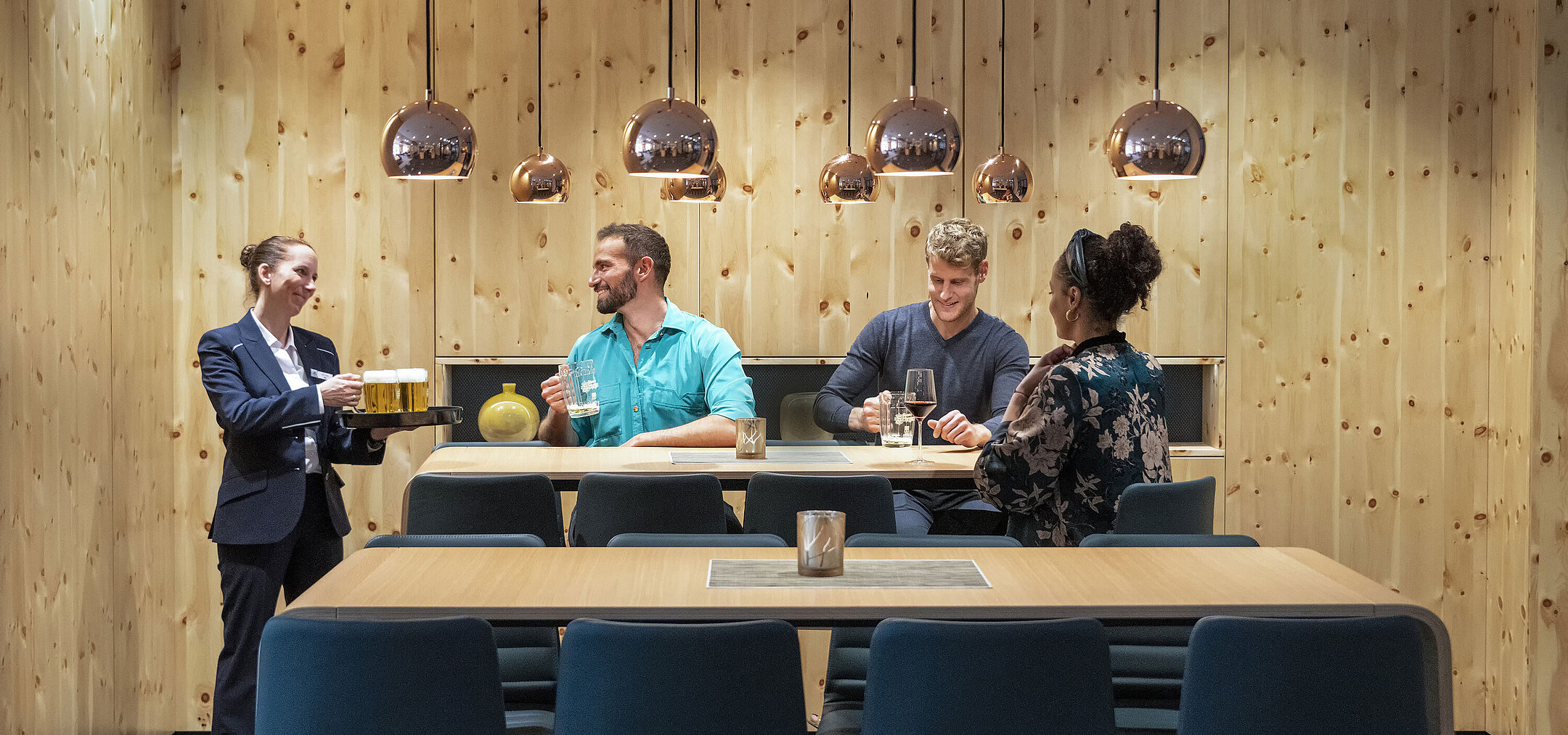Des invités profitent de boissons dans une ambiance chaleureuse tandis qu'une serveuse souriante les sert.
