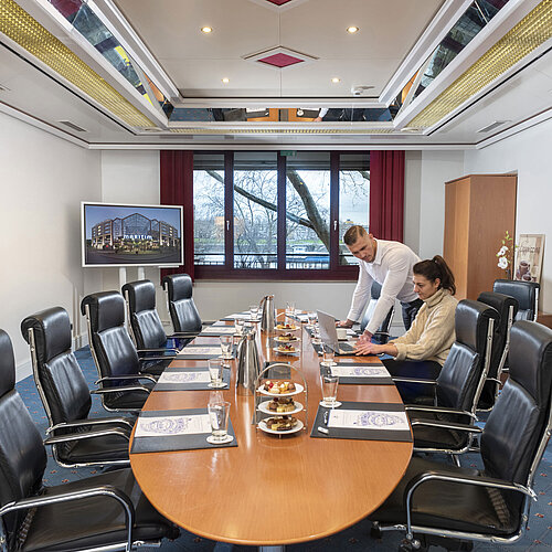 Two people working in the Salon Boardroom at Maritim Cologne with laptops at a conference table with drinks and snacks.