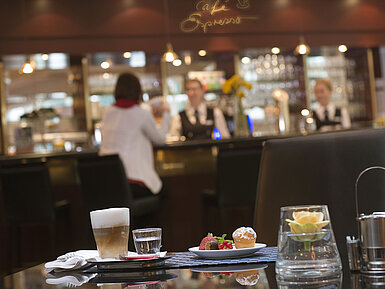 Latte macchiato and pastry at the café in Maritim Hotel Stuttgart with bar view in the background