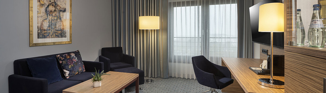 Junior suite en el Maritim Darmstadt con decoración elegante, sofá, escritorio, TV y grandes ventanas para mucha luz natural.