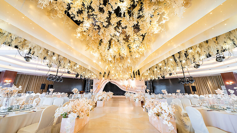 Salón de bodas decorado con un techo floral, escenario elegante y asientos refinados