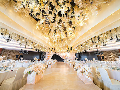 Salón de bodas decorado con un techo floral, escenario elegante y asientos refinados