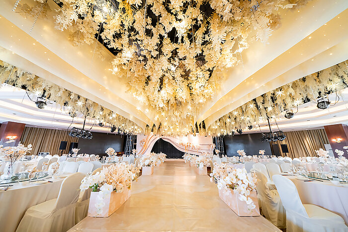 Salón de bodas decorado con un techo floral, escenario elegante y asientos refinados