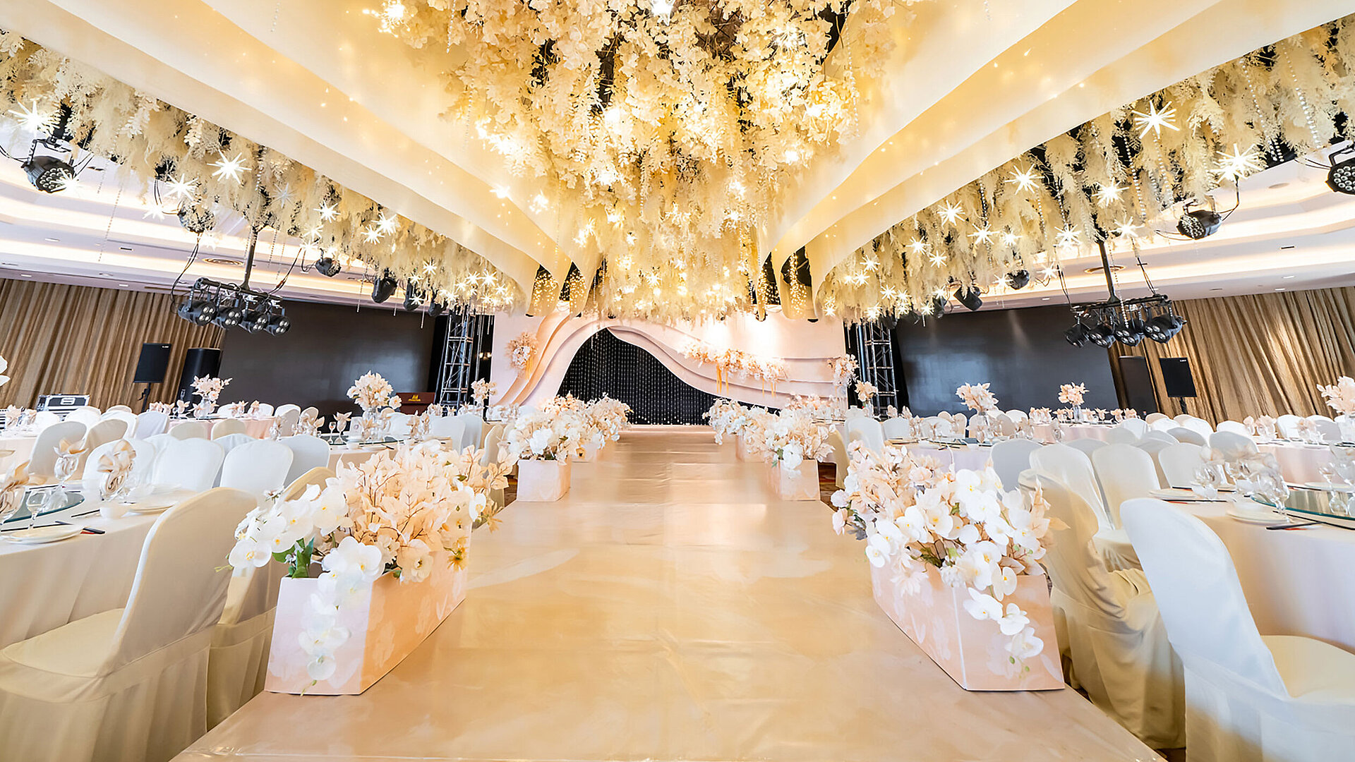 Salón de bodas decorado con un techo floral, escenario elegante y asientos refinados