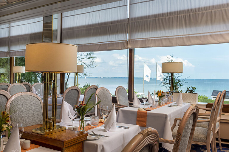 Ristorante elegante con tavoli apparecchiati e vista mare, decorato con lampade e fiori per un'esperienza culinaria raffinata