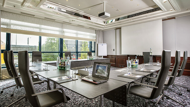 Sala luminosa con mesa grande, sillas de cuero y tecnología moderna.