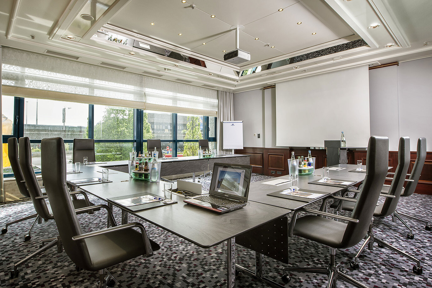 Sala luminosa con mesa grande, sillas de cuero y tecnología moderna.