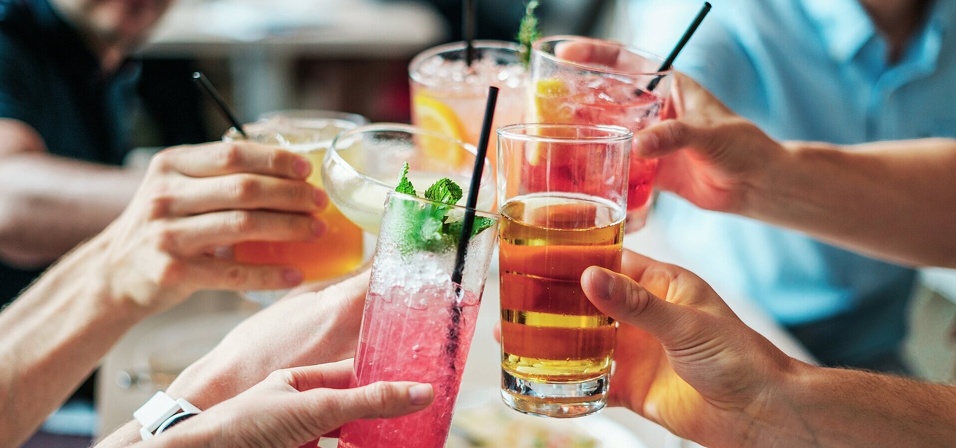 Several people clinking glasses with colourful drinks and cocktails during a social gathering.