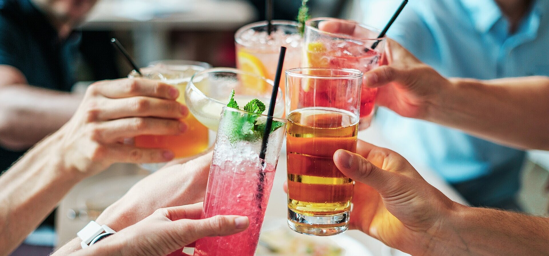 Several people clinking glasses with colourful drinks and cocktails during a social gathering.