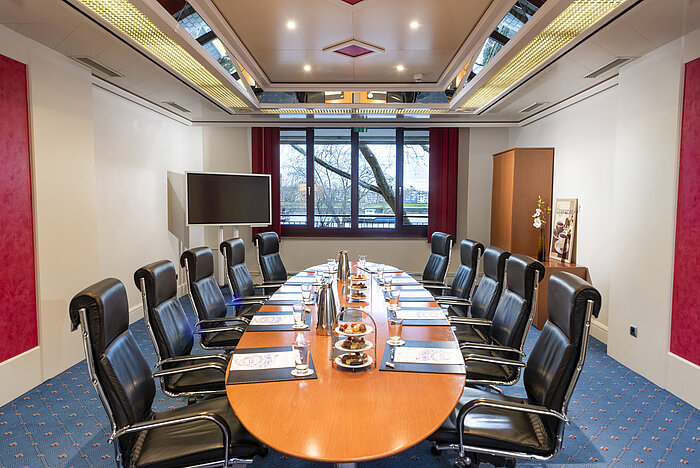 El salón Boardroom en Maritim Colonia, con una mesa de conferencias ovalada, sillas de cuero y materiales de conferencia.
