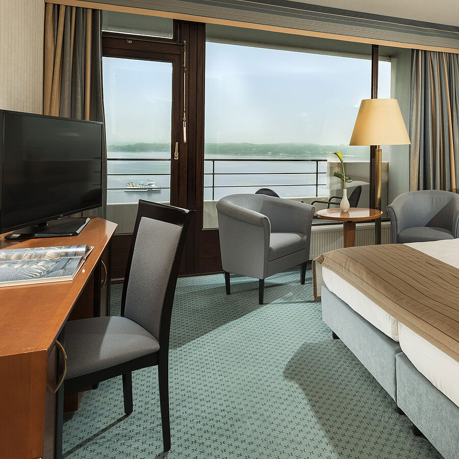 Chambre supérieure au Maritim Hotel Kiel avec bureau, coin salon, grand lit double et balcon avec vue sur le fjord.
