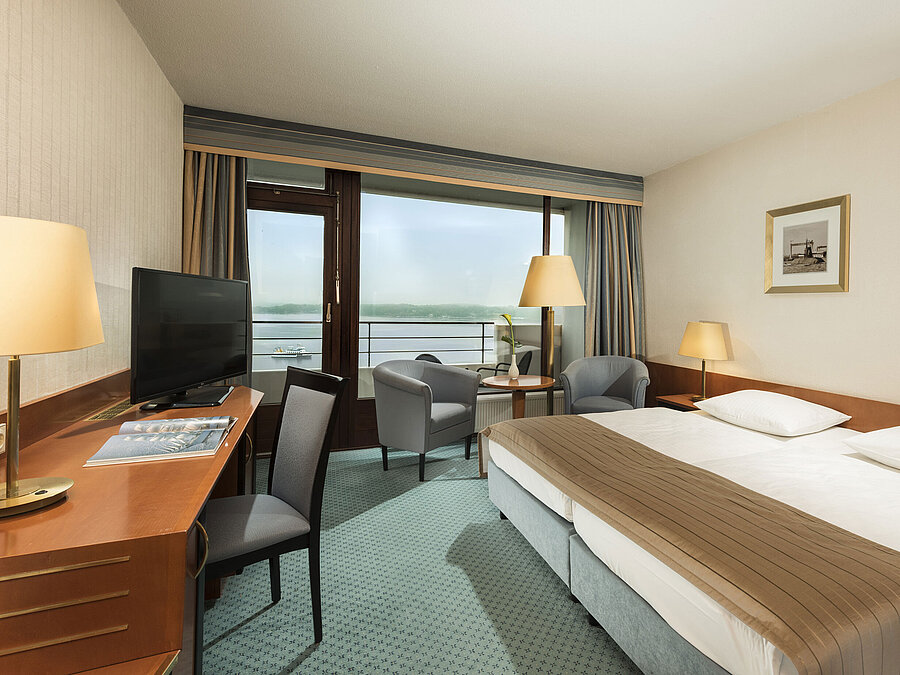 Camera superior del Maritim Hotel Kiel con scrivania, area salotto, ampio letto matrimoniale e balcone con vista sul fiordo.