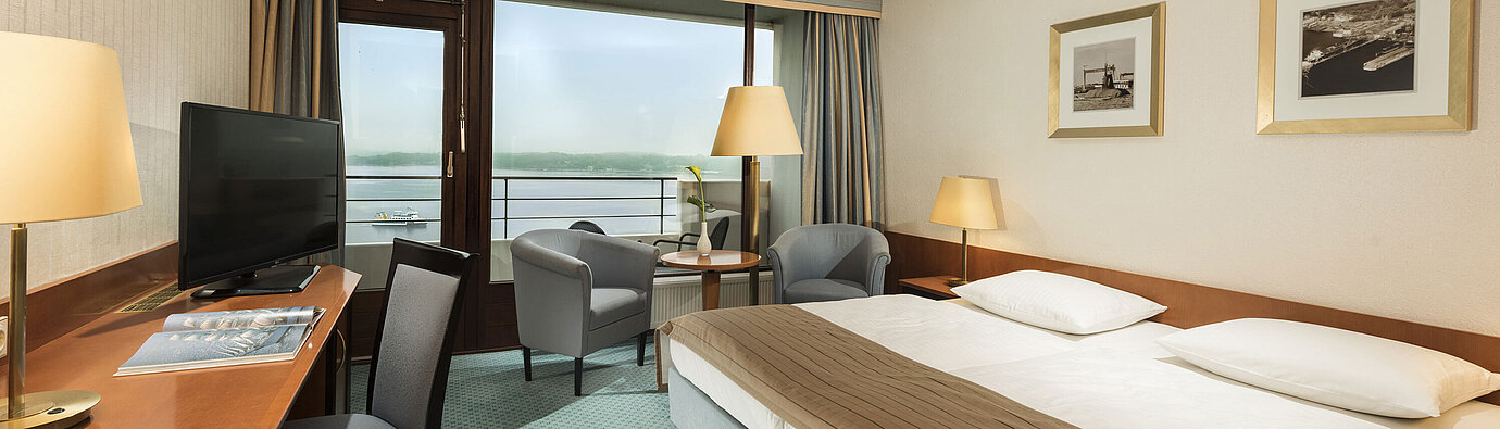 Camera superior del Maritim Hotel Kiel con scrivania, area salotto, ampio letto matrimoniale e balcone con vista sul fiordo.