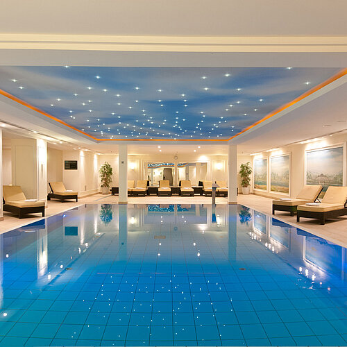 Piscina coperta lussuosa al Maritim Hotel Dresden con lettini e illuminazione suggestiva sul soffitto.