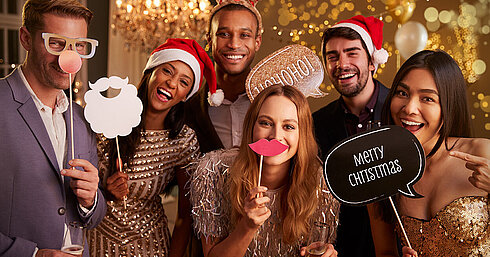 Elegant group celebrating Christmas party with sparkling wine and Santa hats in golden setting