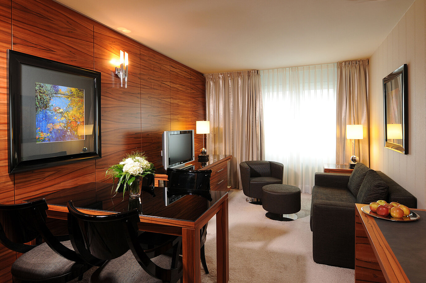 Zona de estar luminosa con sofá, sillón, TV y escritorio en el Maritim Hotel Múnich