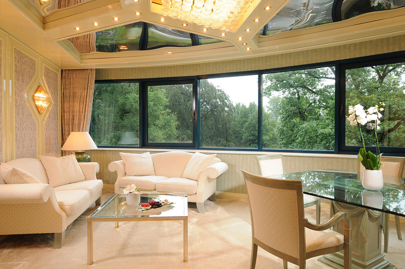 Luxurious Suite with elegant seating, glass dining table, and large panoramic window with greenery view.