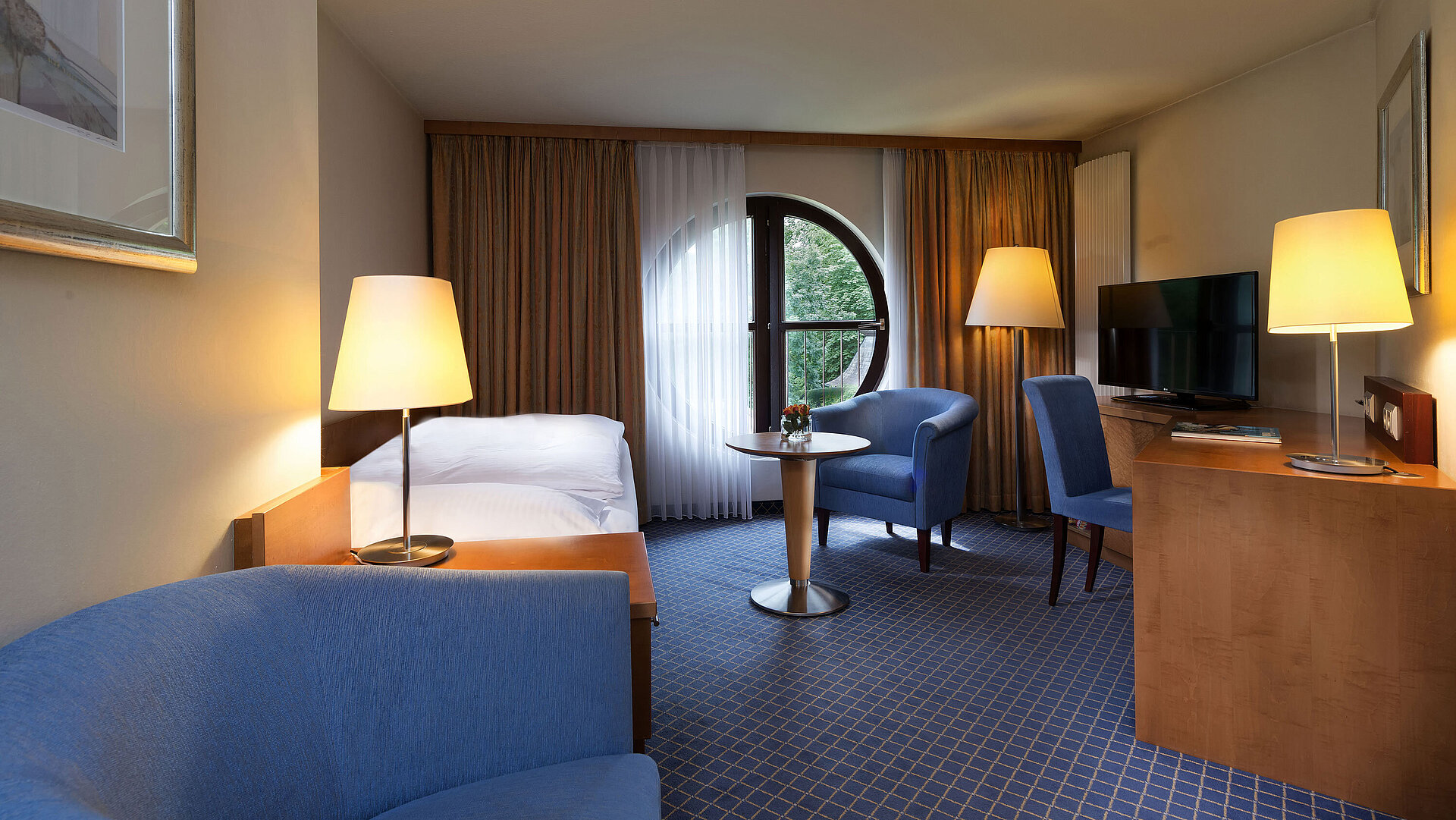 Camera Classic al Maritim Hotel Fulda con letto singolo, scrivania, area salotto e finestra rotonda con vista.