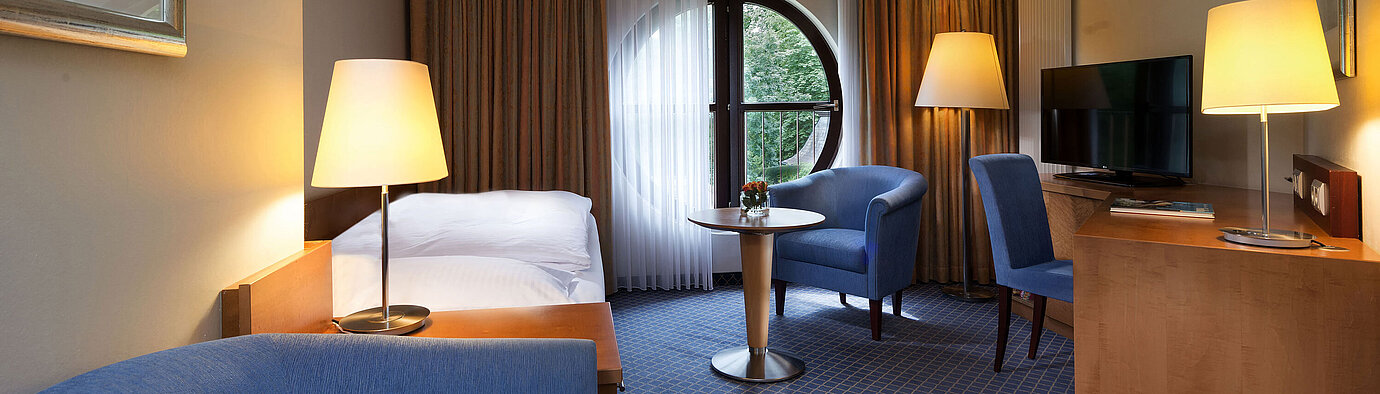 Classic room at Maritim Hotel Fulda with single bed, desk, seating area, and round window with a view.