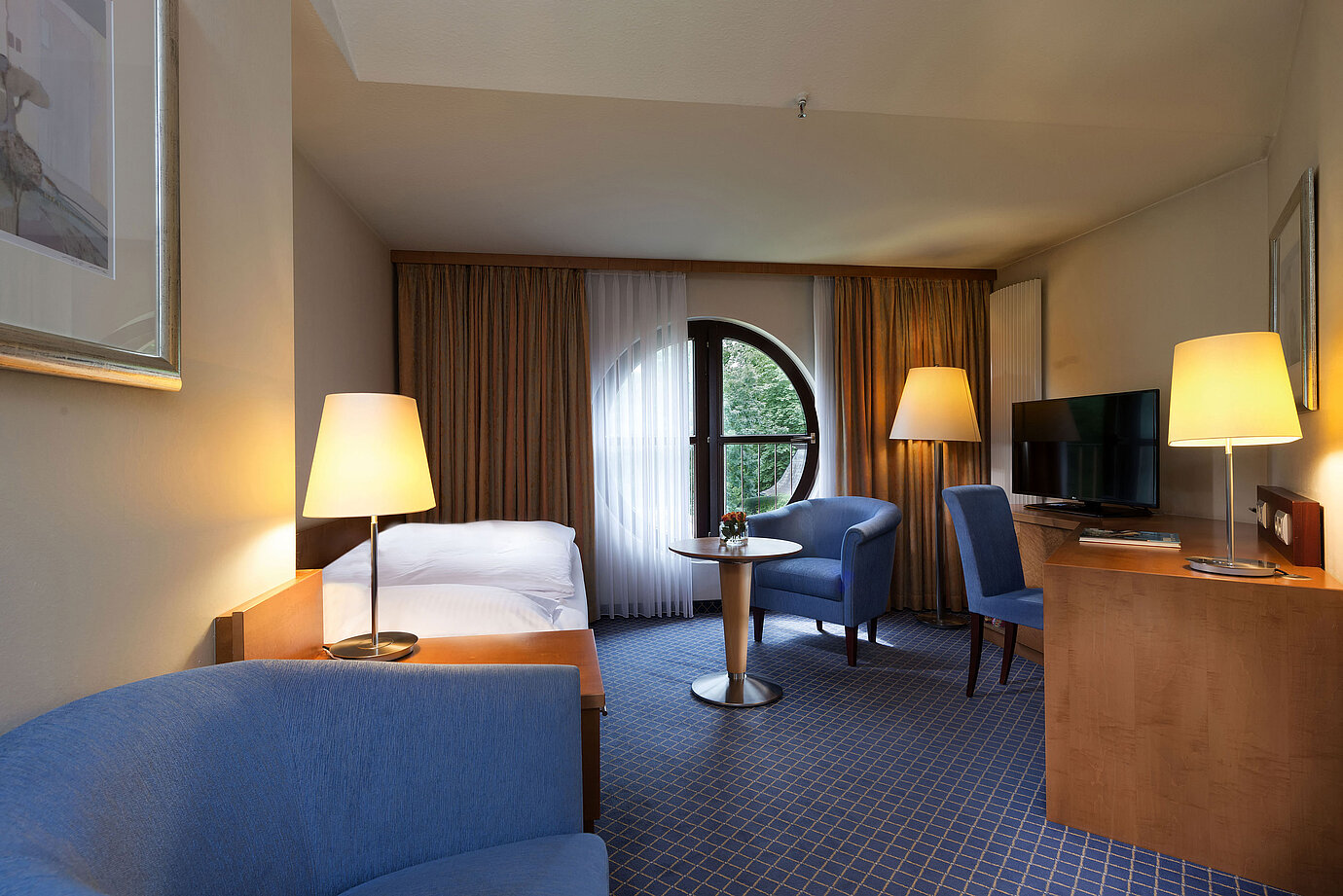 Camera Classic al Maritim Hotel Fulda con letto singolo, scrivania, area salotto e finestra rotonda con vista.