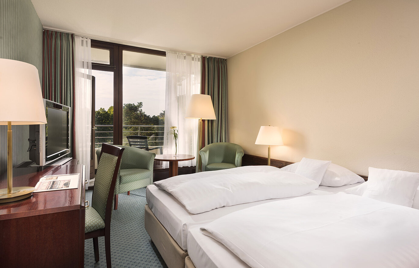 Camera con balcone, scrivania e poltrone al Maritim Hotel Bad Salzuflen