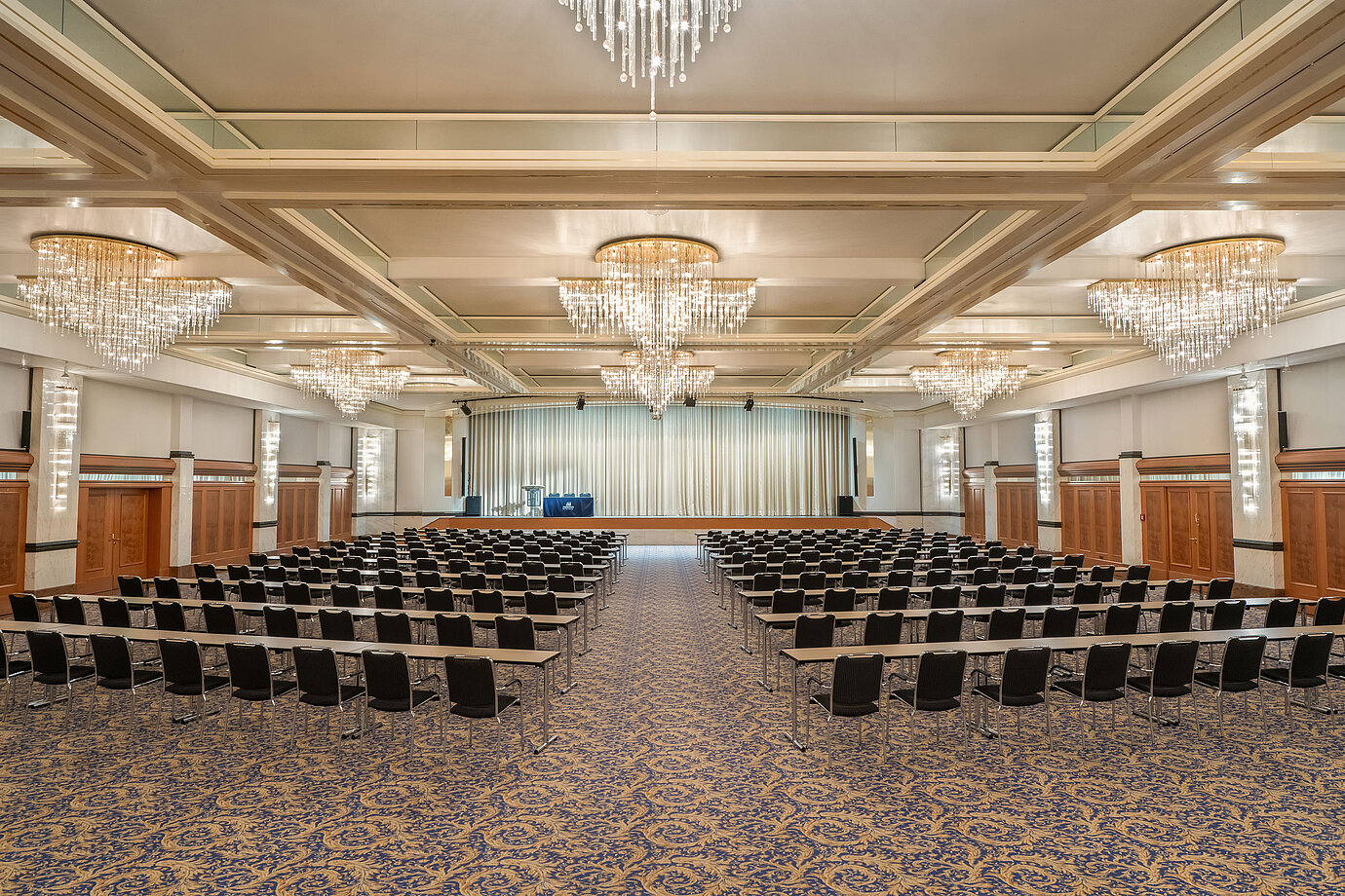 Fürst-von-Metternich Hall with large stage, row seating, elegant chandeliers and bright interior.
