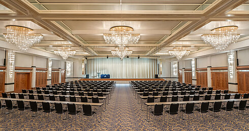 Salón Fürst-von-Metternich con gran escenario, filas de asientos, elegantes lámparas y ambiente luminoso.
