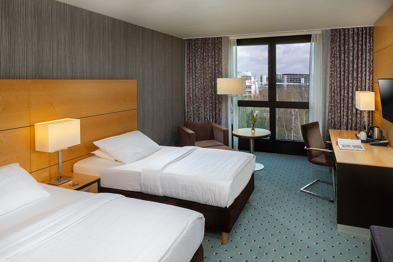 Habitación clásica en el Maritim Düsseldorf con dos camas individuales, escritorio, sillón y ventana con vistas al aeropuerto