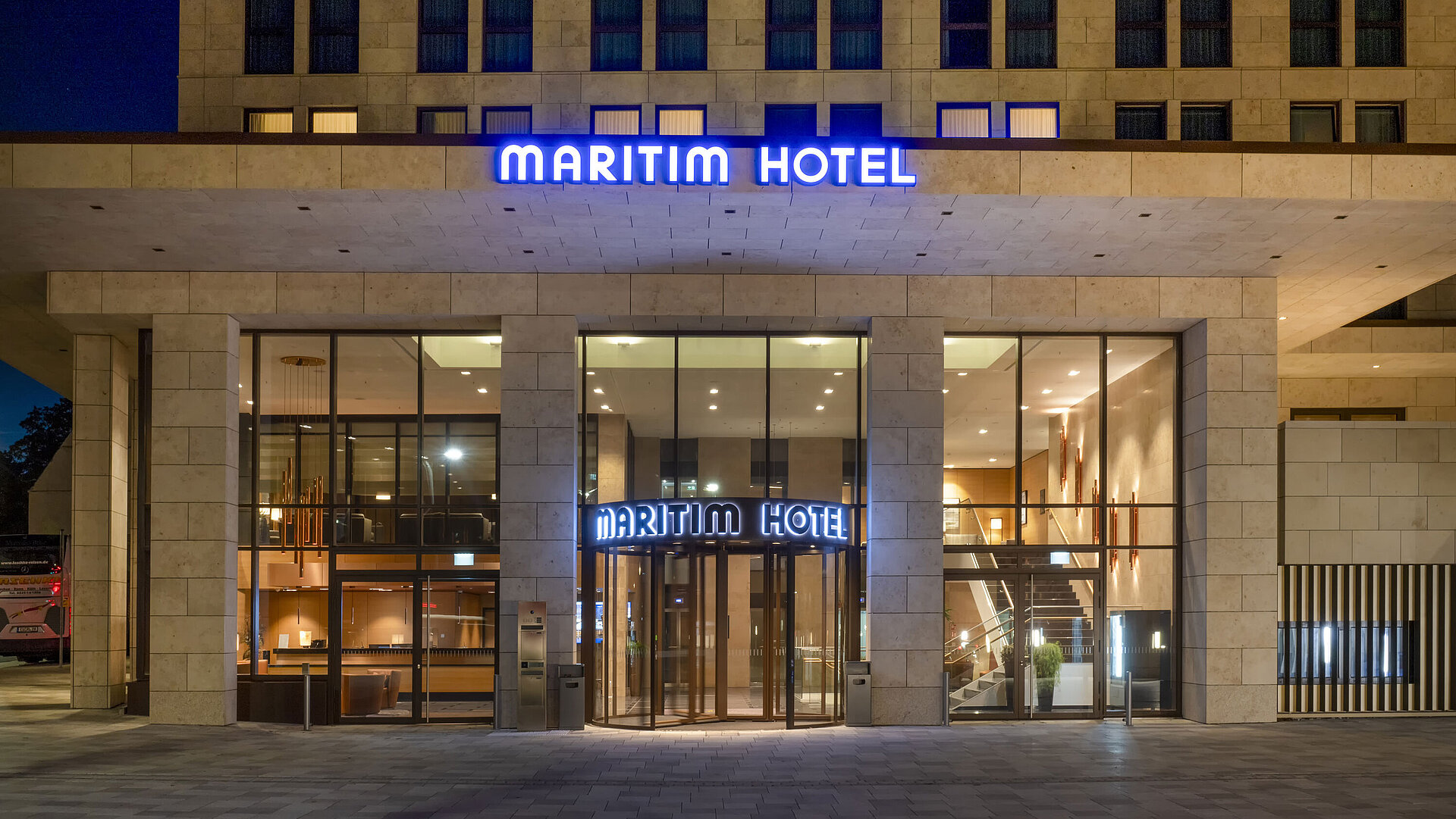 Entrada iluminada del Maritim Hotel Ingolstadt con fachada de vidrio moderna por la noche.