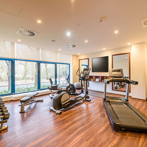 Centro fitness moderno con vista al Maritim Hotel Bremen, con tapis roulant, manubri e attrezzi da palestra.