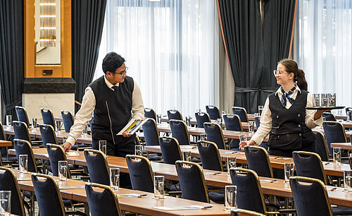 Membri dello staff al Maritim Hotel Magdeburg mentre preparano la sala con bicchieri e materiali sui tavoli.