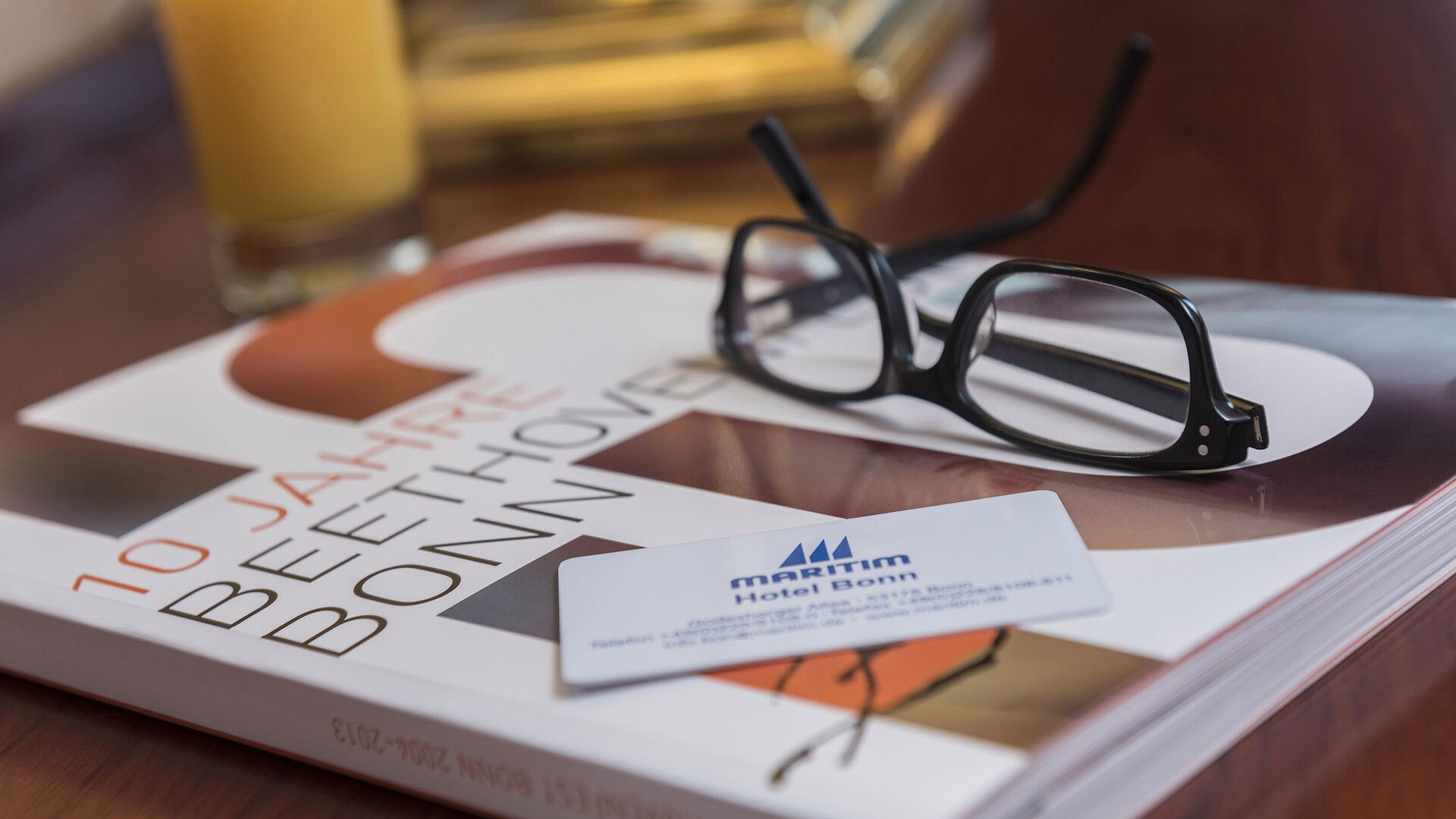 Primer plano de una habitación del Maritim Hotel Bonn con gafas, mapa del hotel y un libro sobre Beethoven.