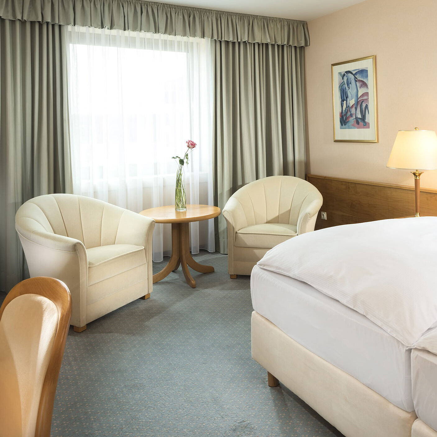 Camera luminosa con due letti, angolo salotto e grande finestra al Maritim Hotel Magdeburg